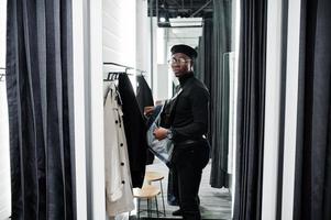 Stylish casual african american man at jeans jacket and black beret at fitting room clothes store change overcoat. photo