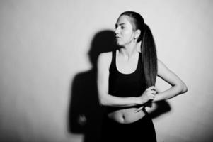 Black and white portrait of beautiful young woman player in sports clothes holding tennis racket while standing against white background. photo