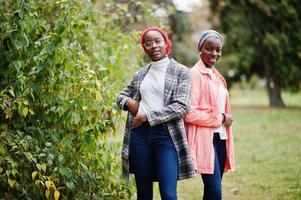 Two young modern fashionable, attractive, tall and slim african muslim womans in hijab or turban head scarf and coat posed at park together. photo