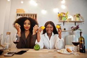 Two african american female friends women spending time at kitchen with wine. Black girlfriends  relaxing at home and having fun with lemons. photo