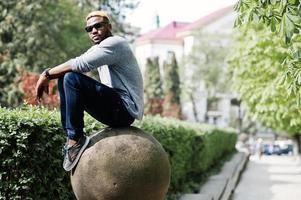 Elegante chico afroamericano con suéter gris y gafas de sol negras posadas en la calle. chico negro de moda. foto