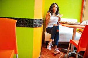 African woman with pizza sitting at bright colored restaurant. photo