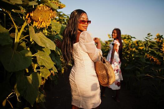 dos jóvenes amigas negras usan pose de vestido de verano en un campo de girasoles. foto