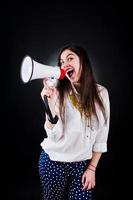 Portrait of a young woman in blue trousers and white blouse posing with megaphone in the studio. photo