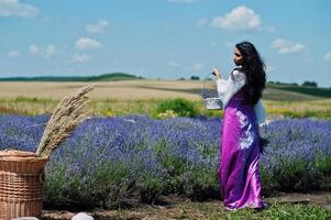 hermosa niña india usa vestido tradicional saree india en campo de lavanda púrpura con canasta. foto