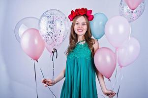 chica feliz con vestido verde turquesa y corona con globos de colores aislados en blanco. celebrando el tema del cumpleaños. foto