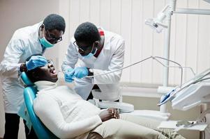 paciente afroamericano en silla dental. oficina de dentista y concepto de práctica médica. dentista profesional ayudando a su paciente en odontología médica. taladrar los dientes del paciente en la clínica. foto