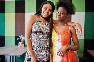 Two black african girlfriends at summer dresses posed in cafe. photo