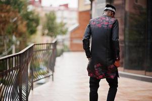 Back of handsome afro american man wearing traditional clothes, cap and eyeglasses in modern city. photo