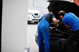 tema de reparación y mantenimiento de automóviles. dos mecánicos uniformados trabajando en autoservicio, revisando el motor. foto