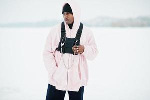 Elegante hombre afroamericano de estilo urbano con capucha rosa posado en un lago congelado en invierno. foto