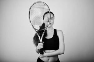 retrato en blanco y negro de una hermosa joven jugadora con ropa deportiva sosteniendo una raqueta de tenis mientras se enfrenta a un fondo blanco. foto