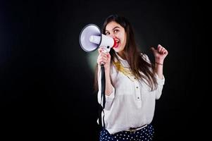Portrait of a young woman in blue trousers and white blouse posing with megaphone in the studio.