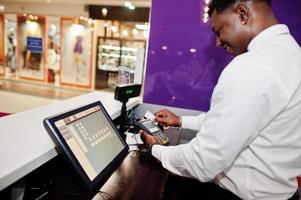 el camarero afroamericano en el bar usa una terminal de tarjeta de crédito en el cajero. foto