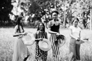 Group of four gorgeous african american womans wear summer hat spending time at green grass in park. photo