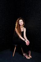 Studio shoot of girl in black on chair with dreads on brick background. photo