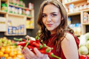 Girl in red holding hot chili peppers on fruits store. photo