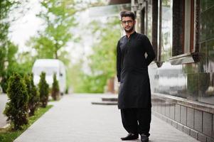 Pakistano bangladesh man wear black traditional clothes and eyeglasses pose outdoor. photo