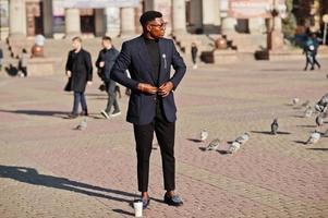 Amazingly looking african american man wear at blue blazer with brooch, black turtleneck and glasses posed at street. Fashionable black guy with cup of coffee. photo