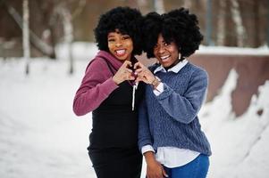 dos mujeres afroamericanas de cabello rizado usan suéteres posados en el día de invierno, muestran el corazón con los dedos. foto