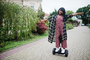 hermosa mujer afroamericana usando segway o hoverboard. chica negra en scooter eléctrico autoequilibrado de doble rueda. foto