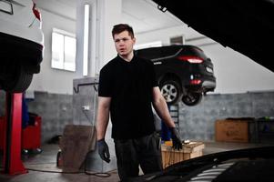 Car repair and maintenance theme. Mechanic in uniform working in auto service, checking engine. photo