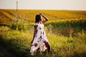 una mujer negra muy joven usa una pose de vestido de verano en un campo de girasoles. foto