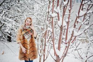 Portraiy of blonde girl in glasses, red fur coat and scarf at winter day. photo