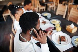 Happy african friends sitting, chatting in cafe and eat food. Group of black peoples meeting in restaurant and have dinner. photo