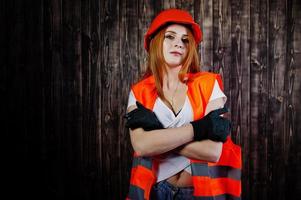 Engineer woman in orange protect helmet and building jacket against wooden background. photo