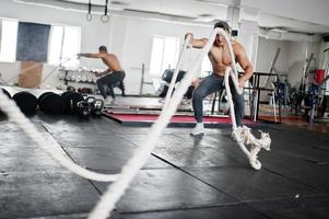 Fit and muscular arabian man working out with heavy ropes in gym. photo