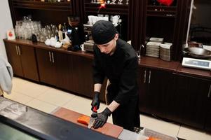 chef profesional vestido de negro haciendo sushi y rollos en la cocina de un restaurante de comida tradicional japonesa. foto