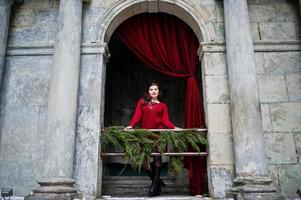 Brunette plus size model at red against arch with curtains. photo