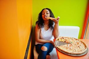 African woman with pizza sitting at bright colored restaurant. photo