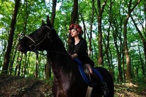 chica mística en ropa de corona en negro a caballo en madera. foto