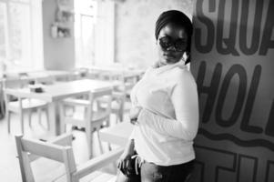 chica musulmana africana con hiyab negro y gafas de sol posadas en un café moderno. foto