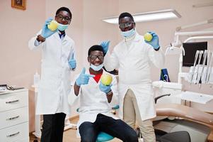 Three african american male doctors colleagues in dental clinic with an apples in hands. photo