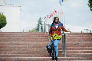 African student female posed with backpack on yard of university, against flags of different countries. photo
