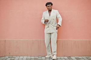 hombre afro con estilo en traje beige de la vieja escuela contra la pared rosa. joven africano de moda con chaqueta informal en el torso desnudo. foto