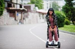 hermosa mujer afroamericana usando segway o hoverboard. chica negra en scooter eléctrico autoequilibrado de doble rueda. foto