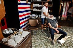 Young bearded man washing head by hairdresser while sitting in chair at barbershop. Barber soul. photo