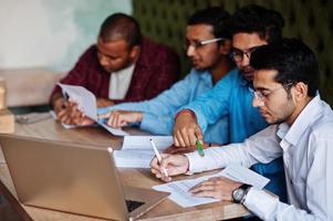 Group of four south asian men's posed at business meeting in cafe. Indians together and sign important documents. Contract to study and work. photo