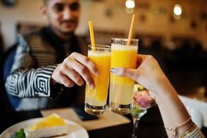 Close up hands of lovely indian couple in love, sitting on restaurant and cheers together by orange juice. photo