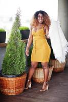 Glamour african american woman in yellow dress and white woolen cape posed at terrace. photo