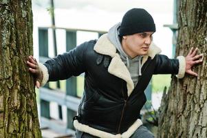 un hombre serio árabe con chaqueta de cuero y sombrero negro copia a su ídolo de la película de acción. foto