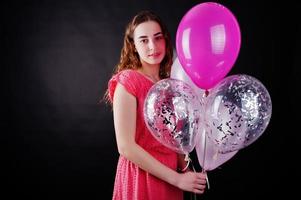 Young girl in red dress with balloons against black background on studio. photo