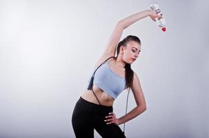 Cheerful attractive young fitness woman in top and black leggings with jump rope and bottle of water isolated over white background. photo