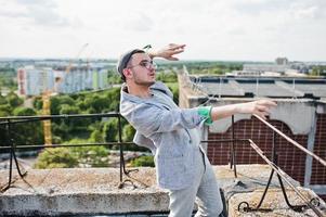 hombre macho con estilo soñador en traje gris, sombrero y gafas posadas en el techo. foto