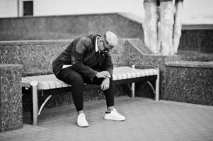 Stylish arabian muslim boy with originally hair and sunglasses posed on streets, sitting on bench. photo