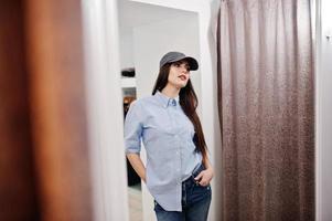 Brunette gorgeous girl in the clothing store boutique at casual clothes and cap against mirror. photo